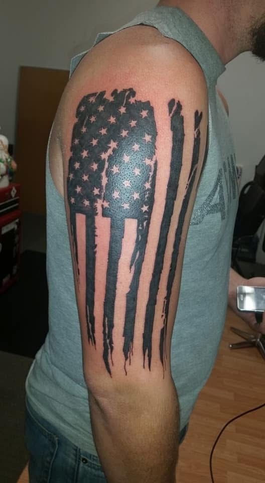 Tattered distressed American flag black and grey upper arm tattoo