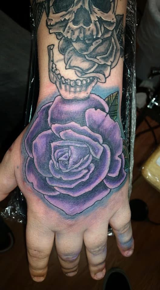 Purple rose with skull above hand tattoo