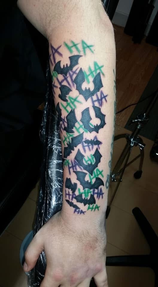Joker bats with HA HA green and purple lettering forearm tattoo