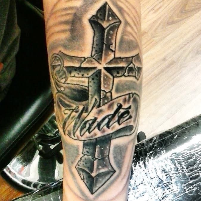 Hade name banner on ornate cross forearm tattoo